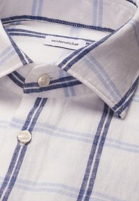 Chemise en lin blanc avec des rayures bleues verticales et horizontales, avec un col classique et des boutons blancs.