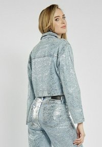 Jasnoniebieska krótka kurtka dżinsowa z srebrnymi błyskotkami; posiada klasyczny kołnierz i długie rękawy. Widoczne koordynujące błyszczące dżinsy.