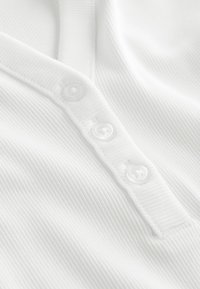 Primer plano de tela blanca acanalada con tres pequeños botones blancos alineados verticalmente en una tapeta.