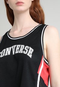 Svart nätbasketlinne med vita och röda accenter, med "CONVERSE" i fet stil över bröstet och en sportig design.
