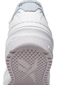 Baskets Reebok blanches avec une semelle en caoutchouc texturée, des accents en daim et des détails de couture. Présente un dessus en cuir lisse et une sangle élastique.
