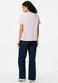 Vaaleanpunainen lyhythihainen t-paita, jossa on punaisia pilkkuja, rento leikkaus ja pyöreä kaula-aukko. Yhdistetty sinisiin leveälahkeisiin farkkuihin.