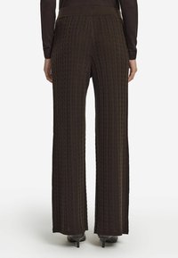 Brązowe dzianinowe spodnie z wzorem w skośne warkocze, szerokimi nogawkami, wysokim stanem i subtelną fakturą. Stylizowane z wysokimi obcasami.