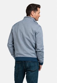 Lichtblauwe zip-up jas met een gestructureerd patroon, geribbelde cuffs en een marineblauwe onderrand, gedragen met donkere jeans.