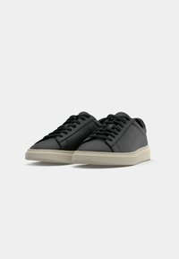 Sorte skinnesneakers med runde tær, flate snører, teksturert overdel og lyse gummisåler. Minimalistisk design uten synlige mønstre.