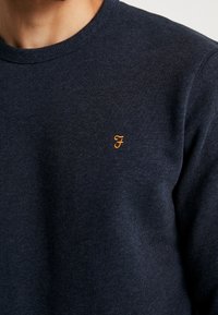 Felpa girocollo blu navy realizzata in tessuto strutturato, con piccolo logo arancione ricamato sul petto, polsini e scollo a coste.