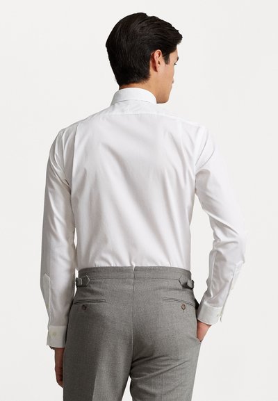Chemise blanche à manches longues avec un col classique, associée à un pantalon gris clair avec des pattes latérales ajustables et deux poches arrière.