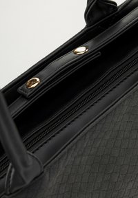 Czarna torebka wykonana z fakturowanej skóry, z zamykanym na zamek przedziałem oraz złotymi detalami, charakteryzująca się eleganckim designem i wyrafinowanym kształtem.