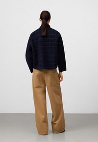 Giacca a quadri blu navy con un fit ampio, abbinata a pantaloni khaki a gamba larga. La giacca presenta un colletto e spalle scese.