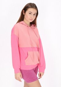 Felpa rosa con un motivo testurizzato, dotata di tasca a marsupio e cappuccio con lacci, abbinata a pantaloni corti rosa. Tessuto morbido, vestibilità rilassata.