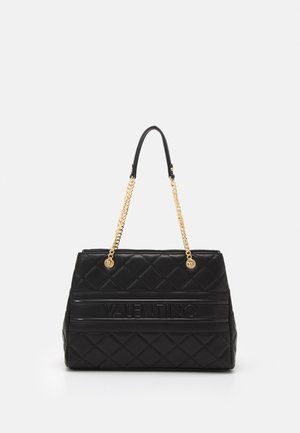 Sac à main noir matelassé avec des chaînes dorées, présentant un logo embossé sur le devant et une forme rectangulaire structurée.