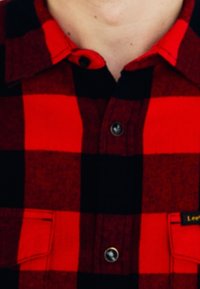 Rot-schwarz karierte Flanellhemd mit einem Knopfkragen, zwei Brusttaschen und schwarzen Knöpfen. Weiche Textur mit klassischem Muster.