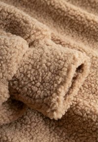 Μαλακό μπεζ ύφασμα sherpa fleece με υφή, με σγουρή επιφάνεια που σχηματίζει πτυχώσεις και σκιές.