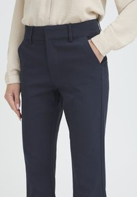 Pantalones ajustados azul marino con una textura suave, corte recto y bolsillos frontales. La cinturilla incluye presillas para cinturón que añaden estilo.