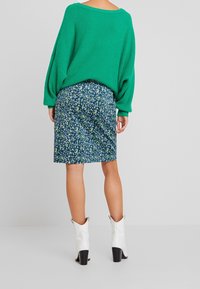 Jersey verde de punto oversize con mangas sueltas, combinado con una falda lápiz ajustada de flores azules. Botines blancos con tacones negros.