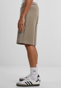 Beige shorts laget av myk stoff, med elastisk midje, sidelommer og en lengde som er litt over kneet, kombinert med sportssko.