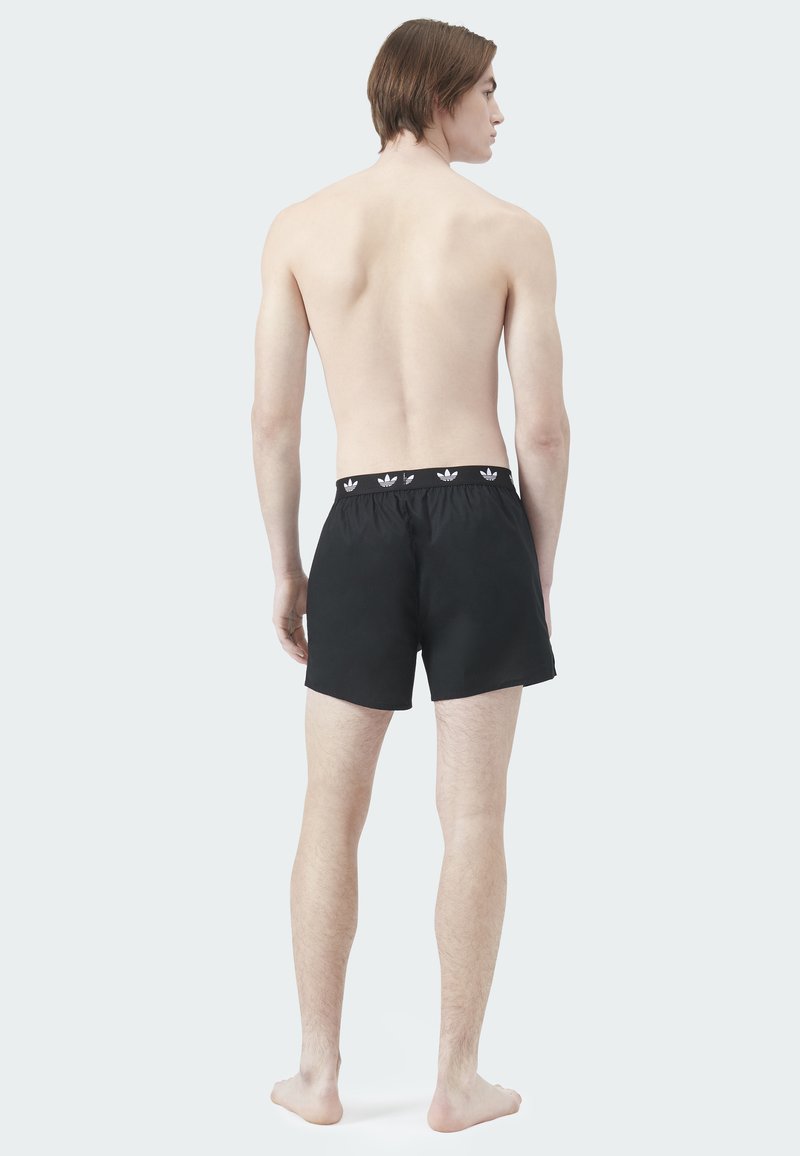 Schwarze Badeshorts mit elastischem Bund und weißem Logomuster. Leichtes Gewebe, über dem Knie geschnitten und glatte Textur.