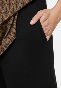 Zwarte broeken met een zijzak, aangevuld met een bruin patroon shirt met abstracte vormen in zwart. Zacht, rekbaar materiaal.