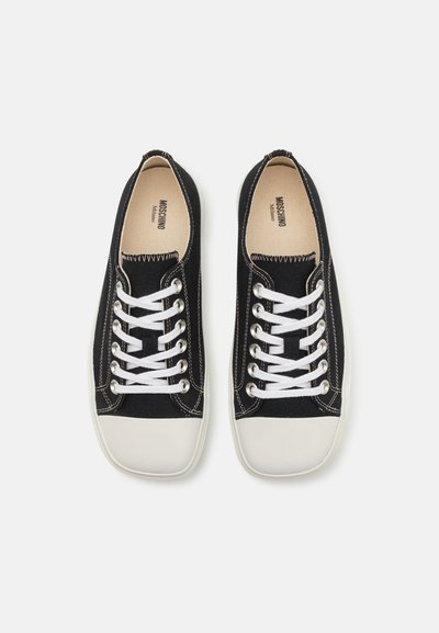 Svarta canvas sneakers med vita snören, texturerad tyg, rund tå och kontrasterande sömmar. Mjukt, platt gummisula i vitt.
