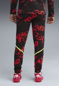 Close-up of a person’s lower body wearing black leggings with red abstract patterns and bright yellow stripes, paired with red sneakers.