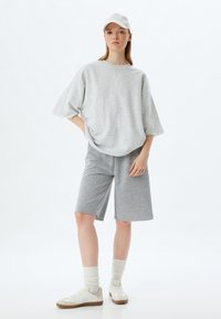 Sudadera gris de gran tamaño combinada con pantalones cortos grises, ambos de una tela suave. Zapatillas blancas y calcetines de color claro completan el look.