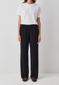 Witte t-shirt met korte mouwen, gecombineerd met zwarte, losse elastische broek. De stof is glad, wat een casual uitstraling creëert. G gedragen met gestructureerde schoenen.