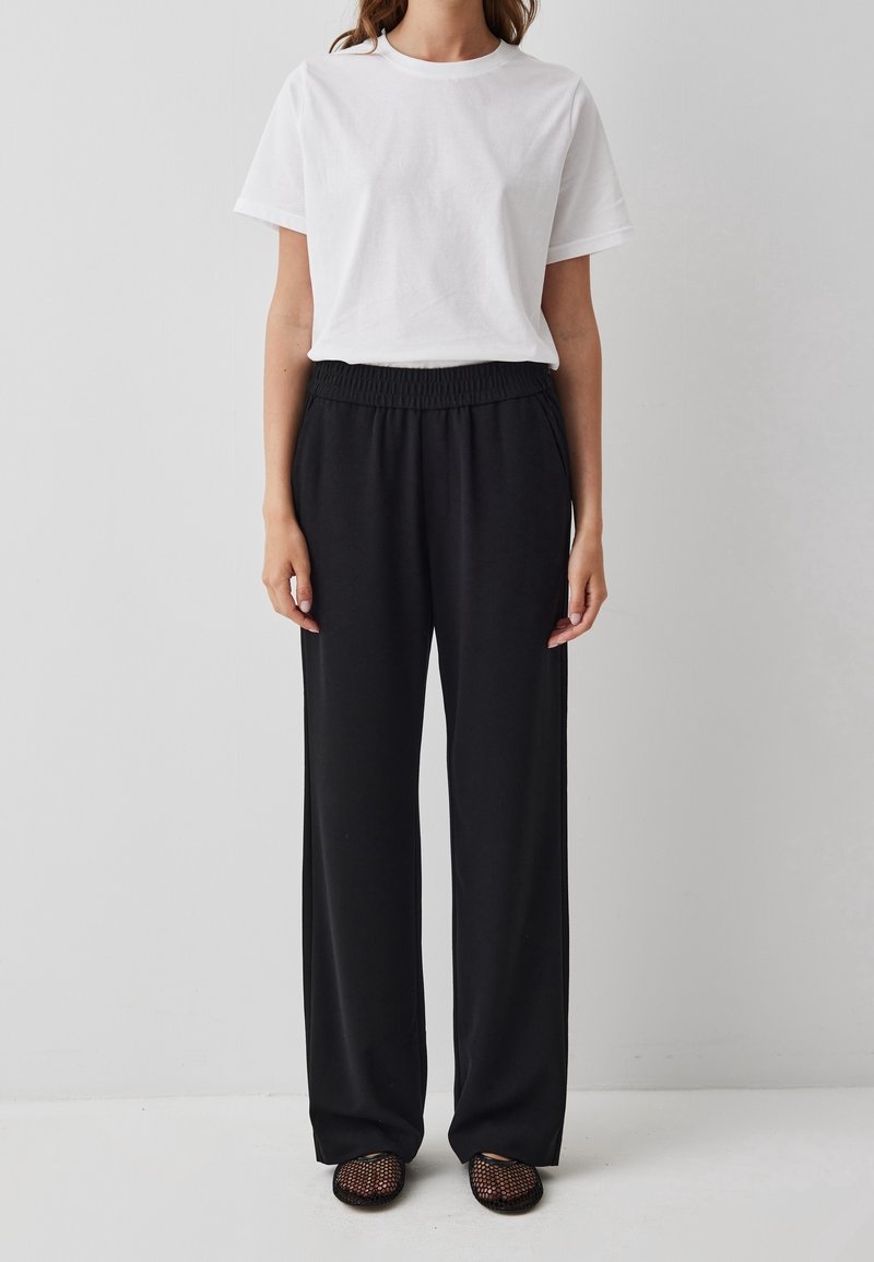 Witte t-shirt met korte mouwen, gecombineerd met zwarte, losse elastische broek. De stof is glad, wat een casual uitstraling creëert. G gedragen met gestructureerde schoenen.