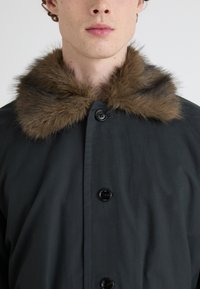 Cămașă neagră cu o guler de blană sintetică maro, având butoane pe partea din față și o textură netedă.