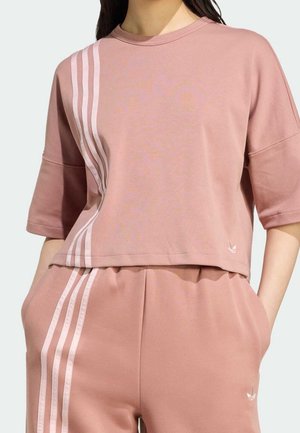 Sweat-shirt court rose avec manches courtes, trois rayures blanches verticales et un petit logo en bas à droite. Tissu à texture douce.