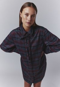 Per dideli, mygtukais užsegamas marškiniai tamsiai burgundiškoje ir jūros perlo raštu. Savybės: smailus apykaklė ir laisvi rankovės. Minkšta medžiaga su laisvu siluetu.