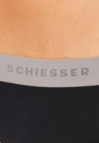 Sous-vêtements noirs avec une ceinture élastique grise. La ceinture présente le mot "SCHIESSER" dans un motif répétitif. Texture lisse.