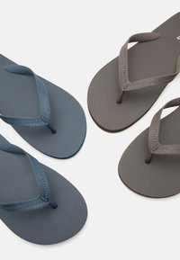 Δύο ζευγάρια υφασμένων σαγιονάρων, ένα μπλε και ένα καφέ, τοποθετημένα διαγώνια σε λευκό φόντο.