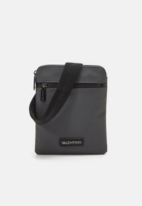 Borsa a tracolla grigia in nylon con chiusura a zip, tracolla nera regolabile e una toppa con logo sul davanti. Texture liscia, design minimalista.