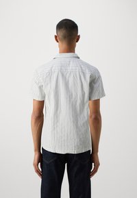 Camisa de manga corta en tejido ligero con rayas verticales azules y blancas, un cuello y un corte recto, presentando una parte trasera con costuras.