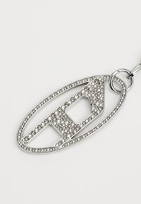 Silver keychain in an oval shape, adorned with small rhinestones. Features a geometric design with an open center and a shiny finish.