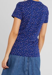 Blue short-sleeve t-shirt with a pink and black leopard print pattern. Soft fabric with a rounded neckline and a fitted design.