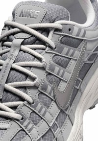 Gros plan d'une basket Nike grise avec des lacets blancs, un mesh texturé, des surpiqûres et le logo Nike swoosh visible sur le côté.