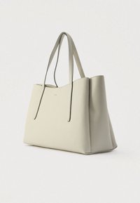 Beżowa torba na ramię ze skóry z dwoma długimi uchwytami, o prostokątnym, usztywnionym kształcie oraz subtelnym logo z przodu. Gładka tekstura.