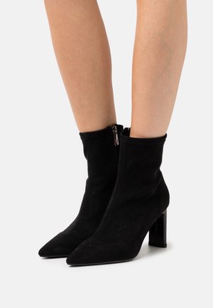 Černé kotníkové boty z broušené kůže se špičatou špičkou, texturovaným povrchem a matným blokovým podpatkem. Mají boční zip pro snadné obouvání.