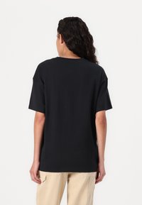Schwarzes Baumwoll-T-Shirt mit lockerer Passform, kurzen Ärmeln und Rundhalsausschnitt, das eine glatte Textur und ein minimales Design aufweist.