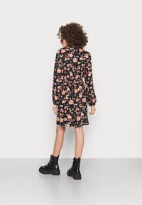 Vestido preto floral com mangas longas, cintura elástica e saia rodada. Apresenta flores rosas e brancas com uma textura de tecido suave. Botas pretas até ao tornozelo.