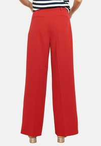 Punased laiad püksid, sileda tekstuuriga, kahel tagataskul ja kohandatud vöökohaga. Komplektis triibuline särk.