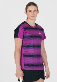 Kortärmad sporttröja i lila och svart, med diagonala ränder, rund halsringning och logotyp på framsidan. Tyget verkar vara lätt.