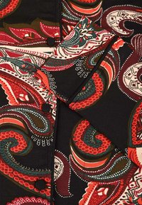 Sort stof med markante paisley-mønstre i rød, grøn, hvid og orange, med stofbetrukne knapper og en foldet manchet.