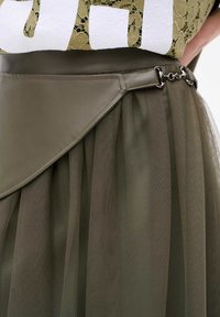 Oliwkowa spódnica z ekoskórzanym paskiem w talii, z warstwowym tiulem z plisami, zabezpieczona metalowymi akcentami.