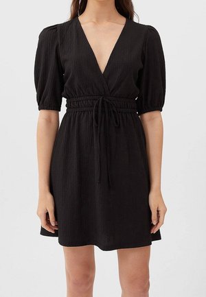 Czarna sukienka z głębokim dekoltem w serek, bufkami na rękawach i paskiem w talii. Wykonana z teksturowanej tkaniny, o luźnym kroju i długości sięgającej ponad kolano.