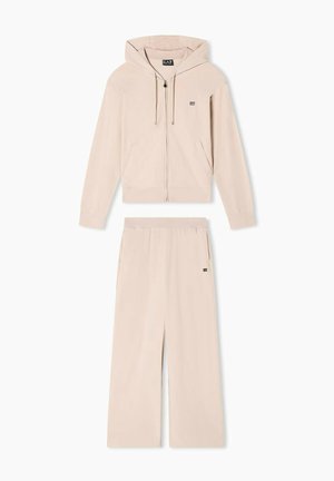 Felpa zip con cappuccio regolabile in beige chiaro, con logo sul petto, abbinata a pantaloni a gamba larga coordinati con tasche laterali.