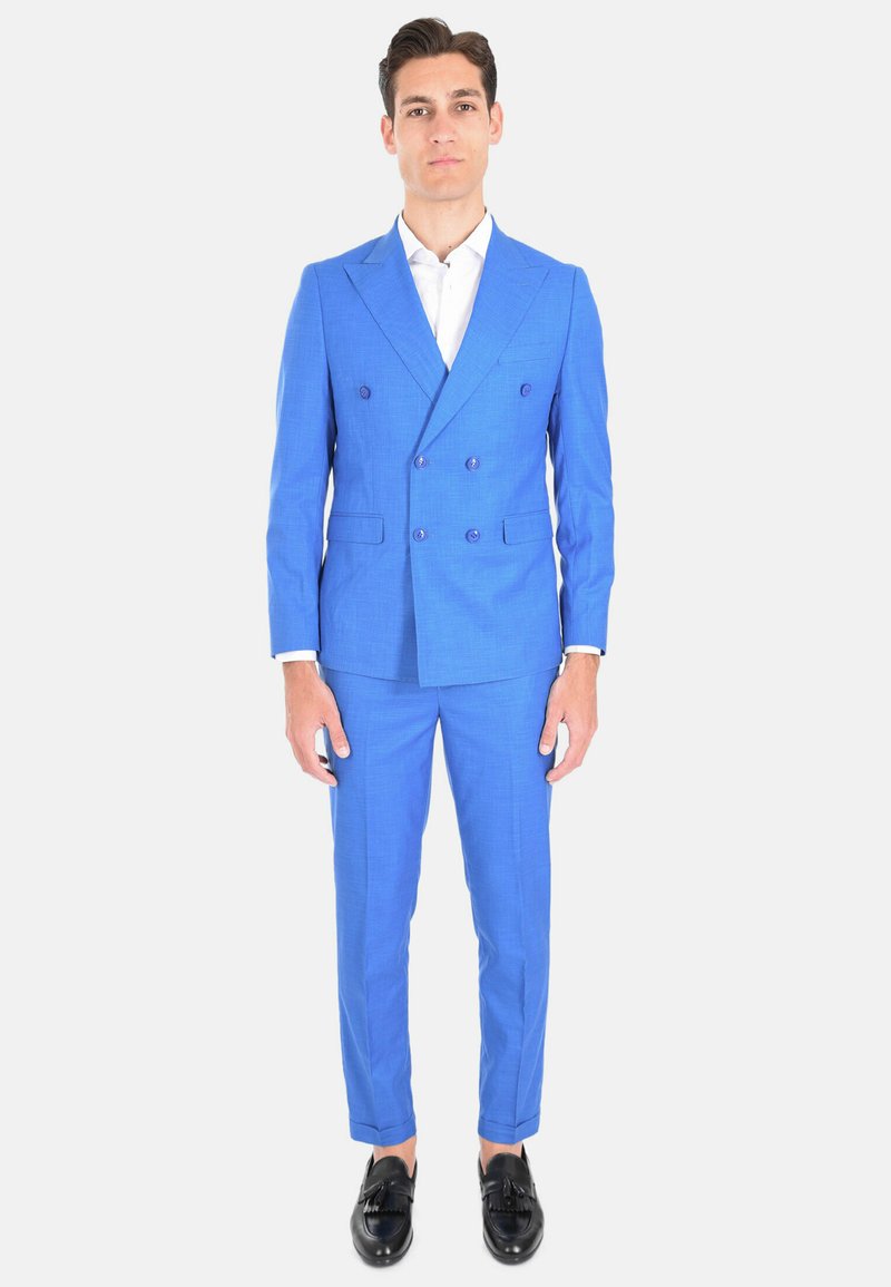 Abito blu doppiopetto con finitura testurizzata, pantaloni slim fit e scarpe nere. Camicia bianca sotto.