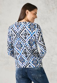 Svetr s dlouhými rukávy v bílé barvě s modro-černým geometrickým vzorem. Hladká textura, kulatý výstřih a přiléhavý střih.
