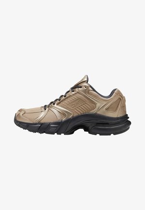 Zapatilla deportiva beige y negra con parte superior de malla y sintética, cordones negros, cuello acolchado y suela negra gruesa y texturizada.